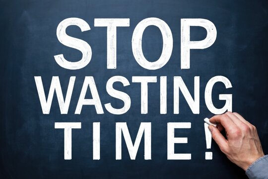 Hand writing stop wasting time in white chalk on a dark blackboard