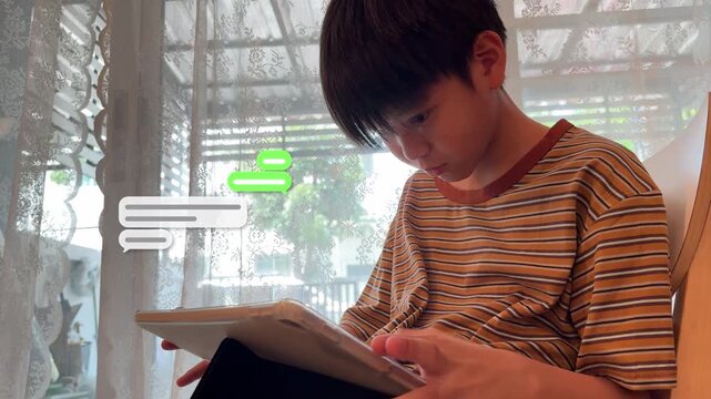 4K footage of a little Southeast Asian boy looking down and working on a tablet device at home with floating chat box animation displays.