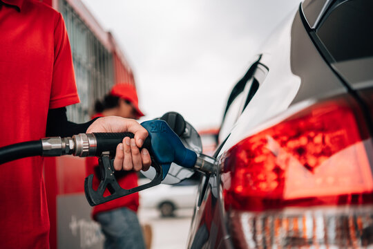 Close-Up of Gas Station Attendant Pumping Fuel into Car.employee's hand securely holding a blue fuel nozzle as it dispenses gasoline into a silver vehicle.