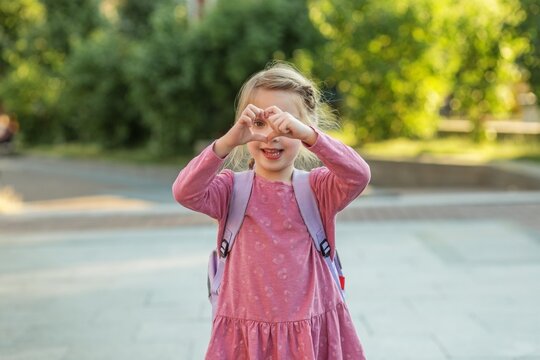 Happy child with backpack making heart shape with hands before school