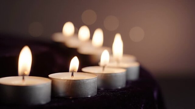 Row of lit tealight candles on a dark surface, showcasing flickering flames and soft bokeh background, creating a warm and inviting atmosphere for relaxation or meditation