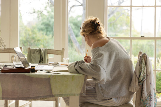 young woman artist using laptop as reference as she does a drawing in her studio