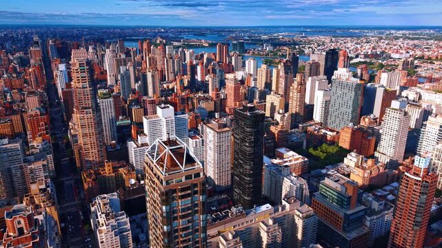 Aerial view of dense skyscrapers in Midtown Manhattan New York. Cityscape of Manhattan buildings extending to East River under clear blue sky.