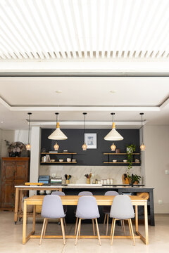 Long wooden dining table with four gray chairs anchoring modern kitchen with marble island