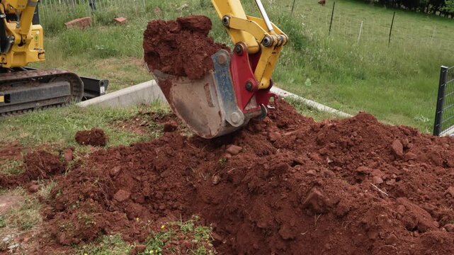Digging deep trench with mini excavator. Excavator bucket extracting soil from hole