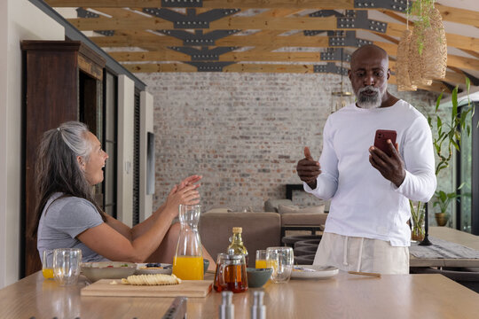 Couple with Senior African American man holding phone at kitchen table with juice, copy space