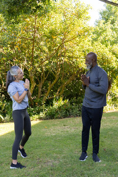 Diverse friends practicing yoga, balancing on one foot in garden, showing smartwatch and shoes