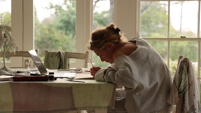 young woman artist using laptop as reference as she does a drawing in her studio