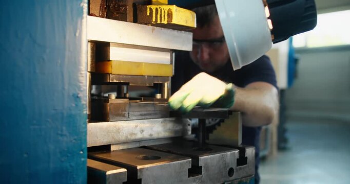 Punch press operator placing metal sheet into die on stamping press, industrial manufacturing process in factory