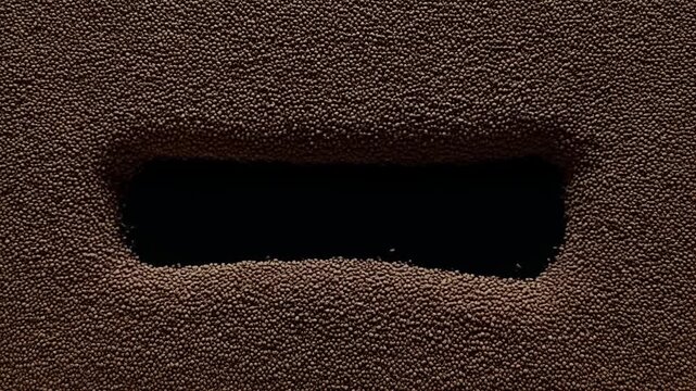 Pan shot of granular beads revealing shifting rectangular void across textured brown surface in closeup studio tabletop