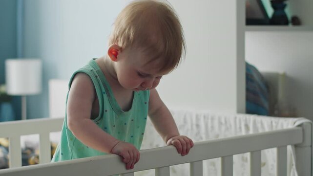 Baby girl holding crib bars and learning to stand upright. Baby milestones include balance, coordination, and body control