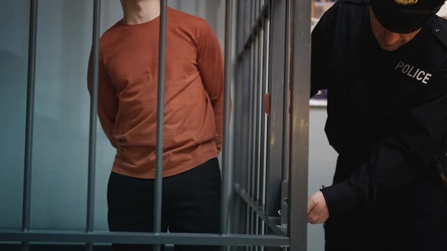 Police officer locking handcuffs and transferring an arrested man from jail cell