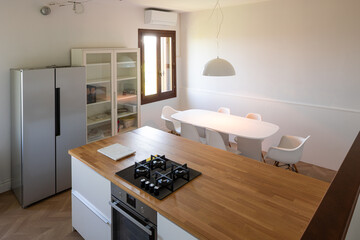 Obraz premium Interior of a recently renovated modern kitchen with an island and gas stove. The floor is parquet. There are six chairs, a white table with a pendant light above it.
