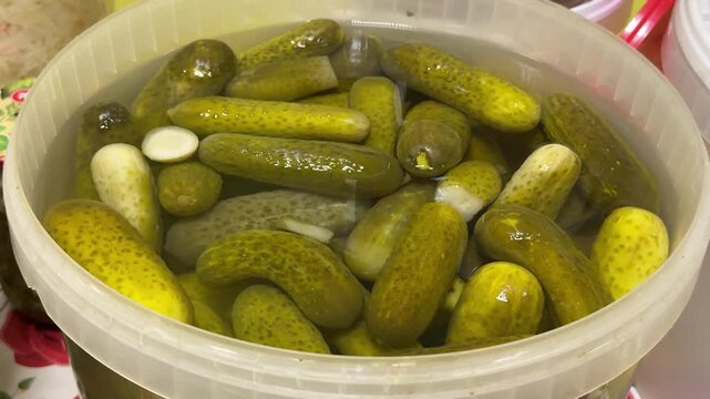 Fresh market pickles in container, closeup of clear plastic tub packed with brined cucumbers, glistening brine