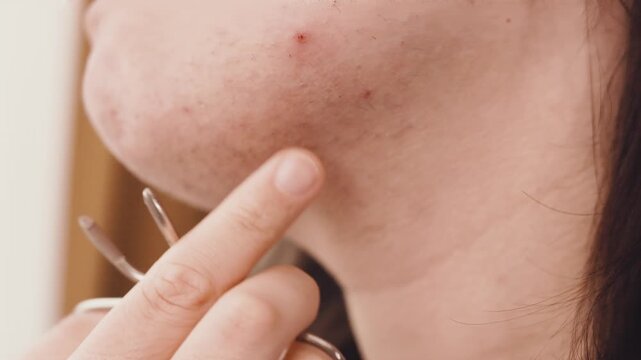 Close-up of a woman checking unwanted facial hair on her chin. She holds scissors for hair removal, highlighting hormonal changes and a home beauty routine. High quality 4k footage
