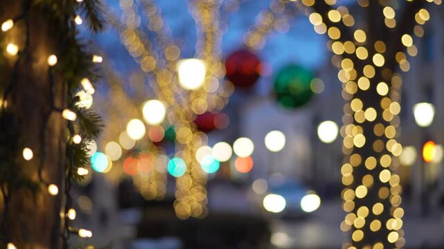 Blurred background of colorful Christmas string lights with bokeh effect on trees outdoors, festive atmosphere.