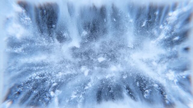 Slow motion overhead zoom tracking shot of powder explosion spreading from black center across icy surface in studio with blue white high contrast lighting