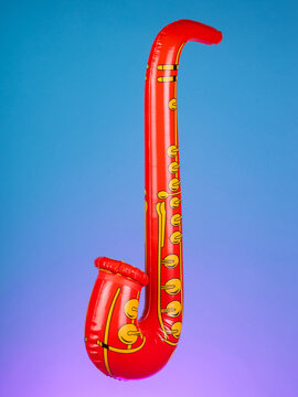 Close-up of a blow-up toy shaped like a saxophone on a purple background, highlighting its bright colors and playful design.