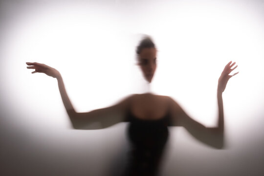 Woman dancing behind frost glass against white background. 