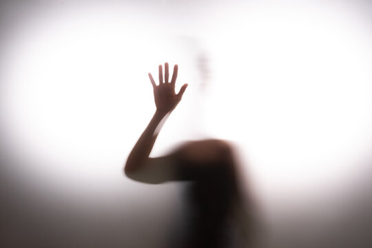 Anonymous person touching frost glass against white studio background. Hope and loneliness concept. 