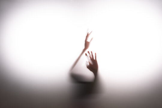 Anonymous person seeking for escape behind frosted glass. Touching it with hands in hope