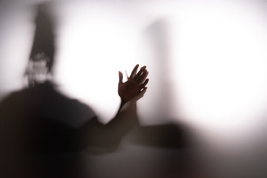 Couple holding hands behind frost glass in white studio space