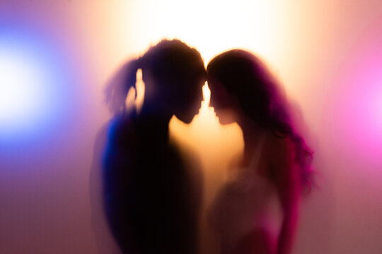 Loving couple sharing a tender moment together in warm light behind frost glass. 