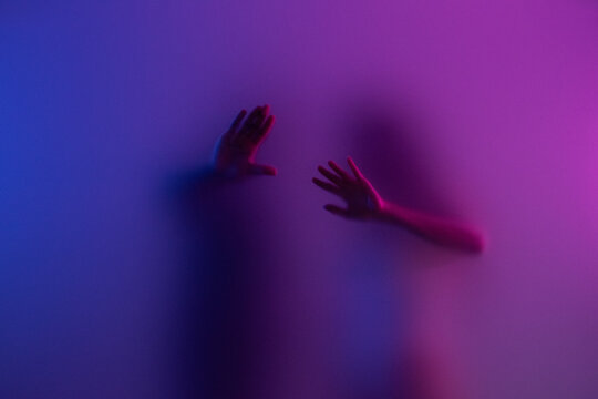 Couple touching frost glass with hands in purple light