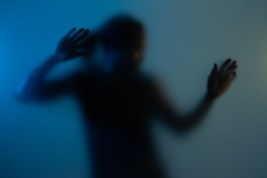 Black American man dancing behind frosted glass at studio. 