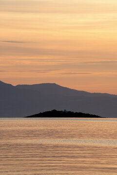 Sunset seascape with Atalanti Island and the small chapel of Agios Nikolaos near Skala Atalantis, Central Greece. Calm Mediterranean waters, layered mountains and pastel evening sky