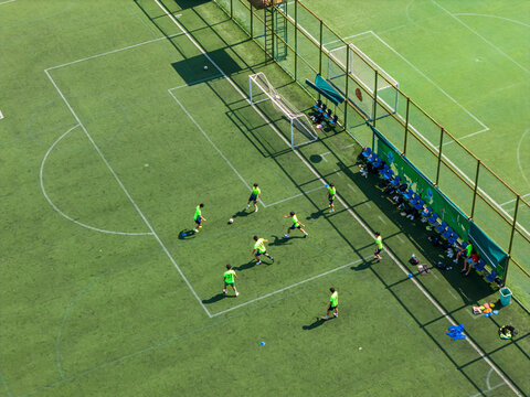 Aerial view of students playing soccer on a green campus field. Promoting physical education and teamwork during break time. Vibrant school sports scene.	