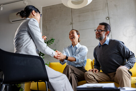 Real estate agent closing a deal with a multicultural couple during a property consultation. Handshake symbolizes trust, agreement, home purchase, and successful partnership