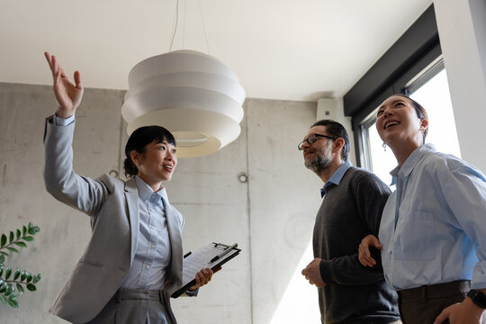 Real estate professional guiding a multicultural couple through a new apartment, discussing relocation, housing options, and investment opportunities in a modern property