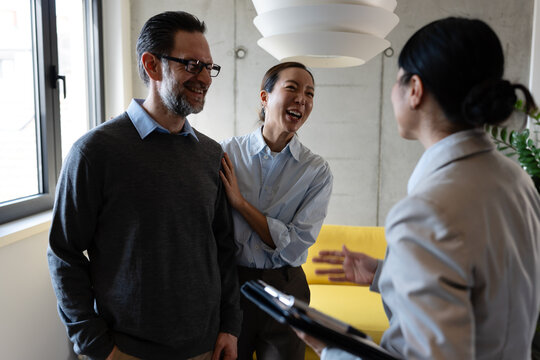 Happy diverse couple on an apartment tour with their real estate agent. Smiling multicultural buyers talking to a realtor, exploring a new property, home, or commercial space to rent or buy.