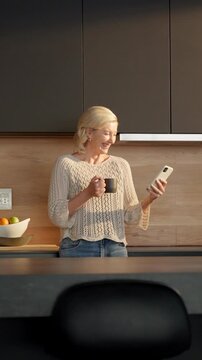Coffee, woman and laugh with phone in kitchen for internet meme, funny online video and streaming. Beverage, mature person and happy with mobile in home for reading comic status, social media or joke