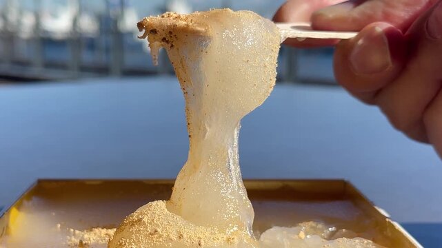 きな粉をトッピングした和菓子のわらび餅。食べたいけど切れず、力強く伸びているわらび餅のクローズアップ動画。