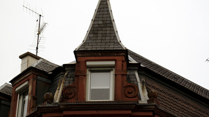 Obraz premium Traditional European house roofs with red tiled roofing, dormer windows, and weathered architectural details create a classic old-town cityscape. The composition highlights historic residential roofto
