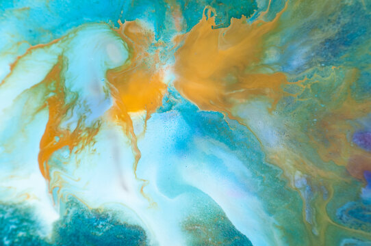 Swirls of blue and orange create a pattern on a canvas in an art studio