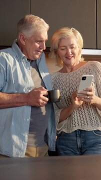 Laugh, coffee and couple with phone in home for internet meme, funny online video and bonding. Tea, mature people and happy with mobile in kitchen for reading comic status, healthy marriage and joke