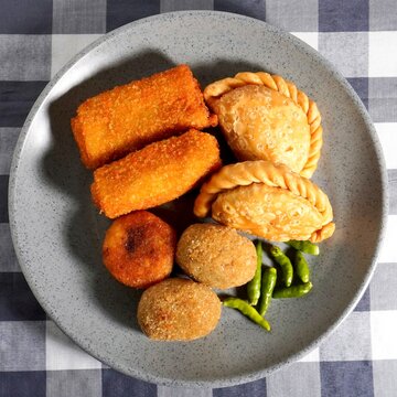 Fried pastel, risoles, and croquette Indonesian traditional snack with green chilli pepper on gray plate isolated on checkered gray background from top angle view.