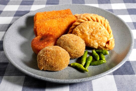 Fried pastel, risoles, and croquette Indonesian traditional snack with green chilli pepper on gray plate isolated on horizontal checkered gray background.