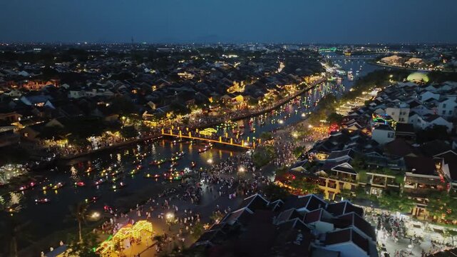 Drone view of crowded riverfront celebrations and colorful boats in Hoi An during the evening.