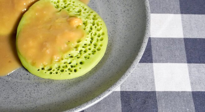 Green serabi cakes with durian and palm sugar sauce isolated on horizontal gray plate and checkered square table background with copy space.