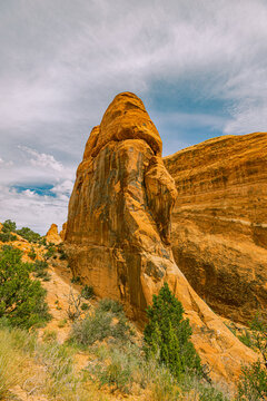 Tall isolated orange sandstone spire tower rising above desert scrub and sagebrush under partly cloudy sky, Devils Garden, Arches National Park, Utah.