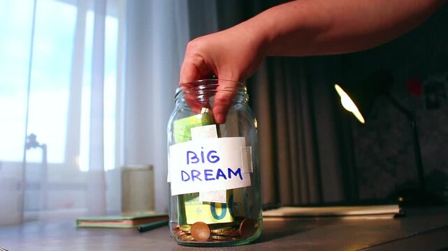 Close up of transparent money jar labeled for BIG DREAM. Represents traditional saving methods and conscious money management for future