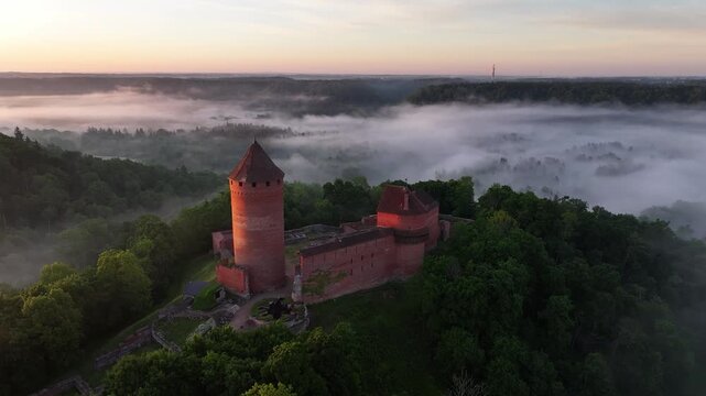 Aerial sunrise view of Turaida Castle rising above morning fog in Gauja National Park, Sigulda, Latvia