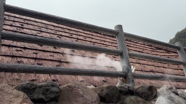 Volcanic geothermal steam rising around traditional thatched roof huts in Beppu Japan