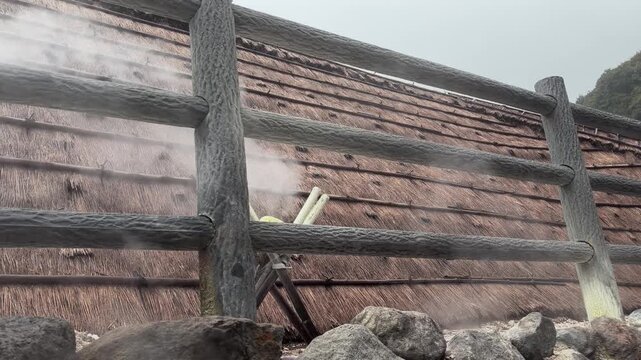 Volcanic geothermal steam rising around traditional thatched roof huts in Beppu Japan