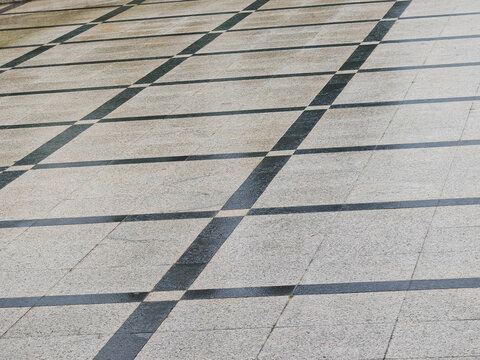 a clean outdoor public plaza floor made from light gray granite paving stones with intersecting dark accent stone bands in a geometric grid layout
