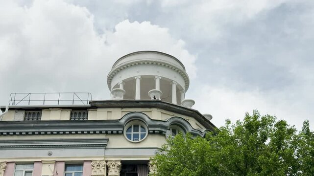 A grand white rotunda crowns an old building facade near green trees. This elegant historical view inspires a peaceful feeling of nostalgia and calm admiration.